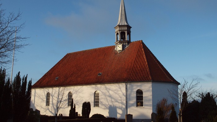 En hvid kirke med rødt tag og tårn mod en klar blå himmel