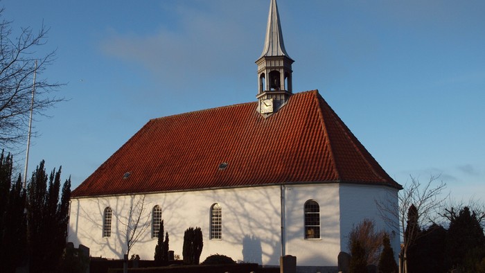 En hvid kirke med rødt tag og tårn mod en klar blå himmel