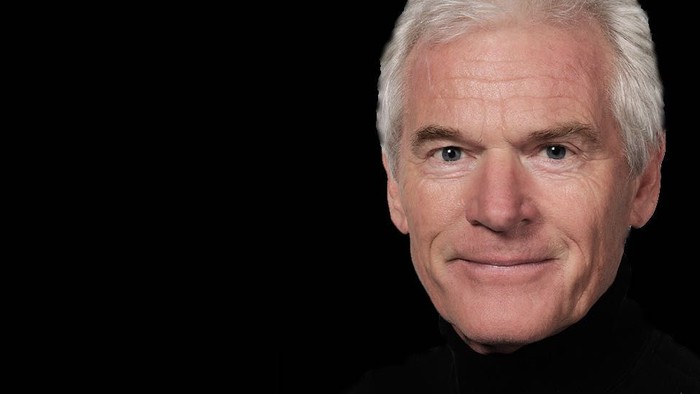 En smilende, eldre mand med kort hår og mørke klæder.