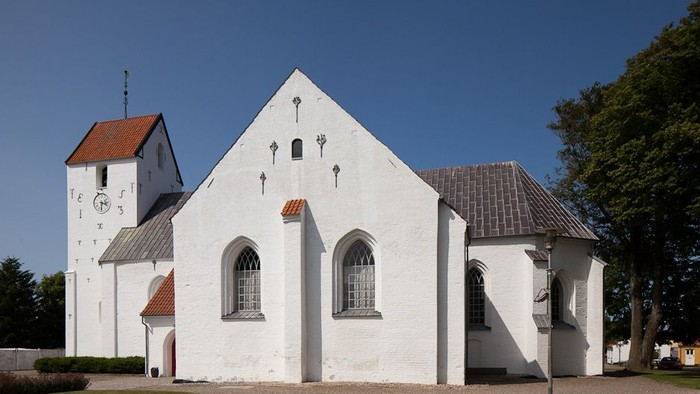 Hvid kirke med spids tak og klokketårn ved siden af
