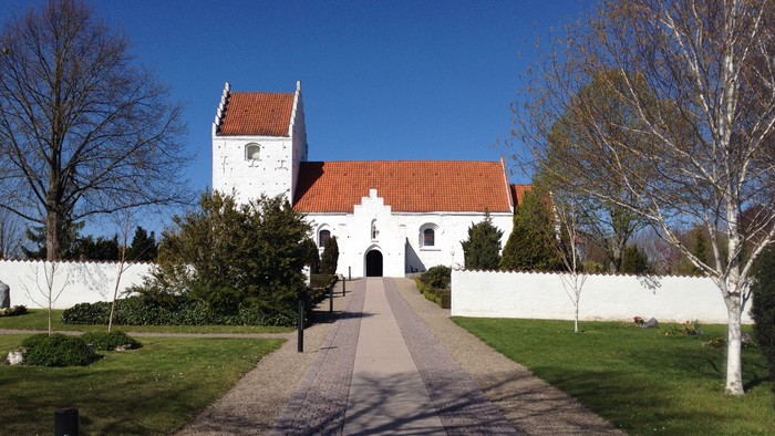 En smuk hvid kirke med rødt tag og en lang gangvej frem til indgangen