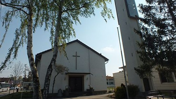 Weiße Kirche mit hohem Turm und Kreuz vor Baum