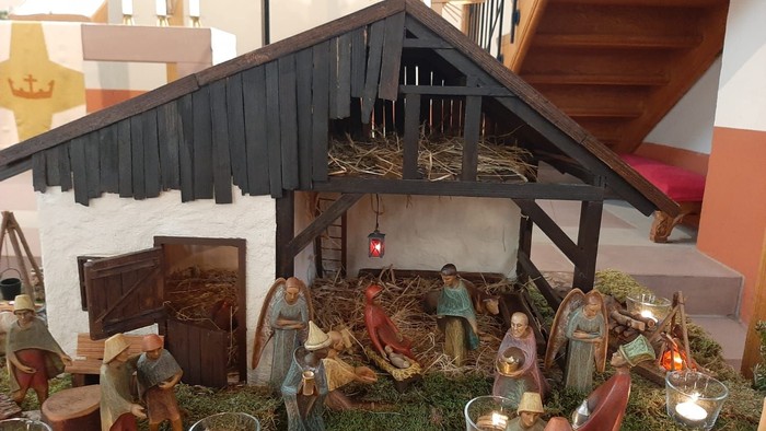 Eine detailgetreue Krippe mit vielen Figuren und einem Stall, beleuchtet durch Kerzen.