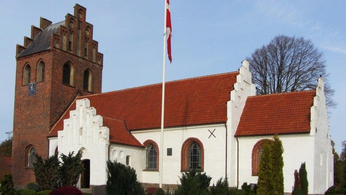 En hvid kirke med rødt tag og en tårn med en dansk flag.