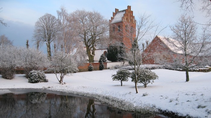 Snødekte træer og hus med refleksion i vand.