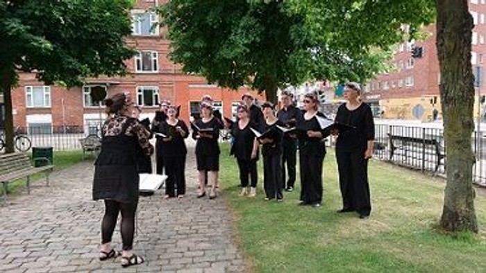 En gruppe korister optræder udendørs ved et træ.