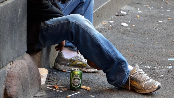 En person sidder på en vegg med en øl i hånden og en sko i vejen.