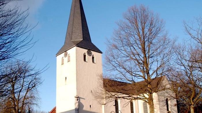 Weiße Kirche mit hohem Turm und spitzem Dach vor blauem Himmel