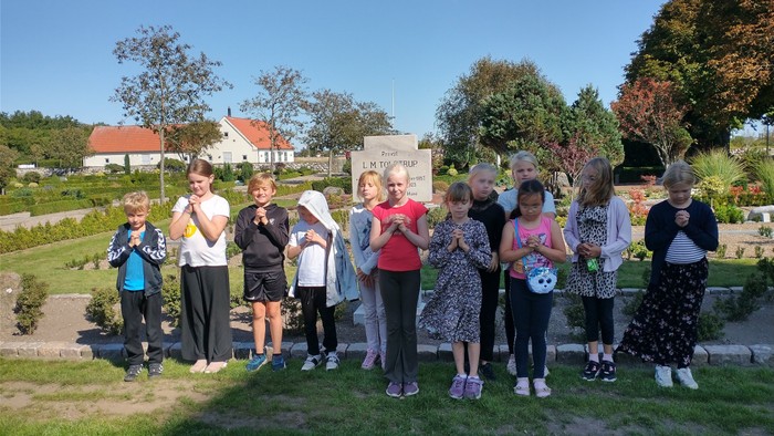 En gruppe børn står sammen udendørs ved en stenmur, alle med blomster i håret