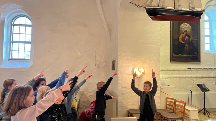 En gruppe af mennesker hyber sig i en kirke, mens en skibsmodell hænger fra taket.