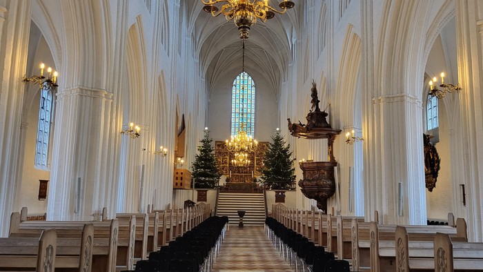 Indre del af en stor, belyset kirke med høje buevægge og træbænke.