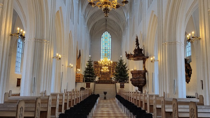 Indre del af en stor, belyset kirke med høje buevægge og træbænke.