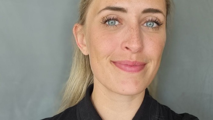 En kvinde med blondt hår og blå øjne smiler til kameraet.