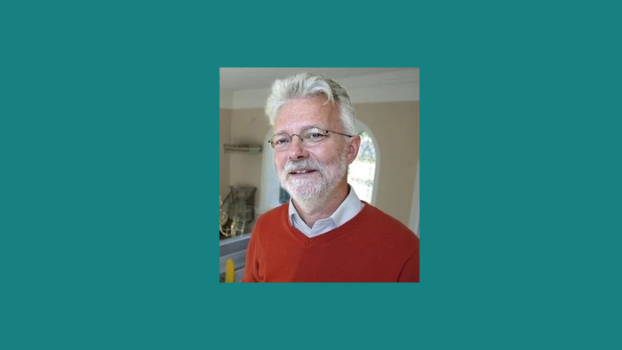 En smilende, eldre mand med hvidt hår og skæg, der bærer en rød trøje.