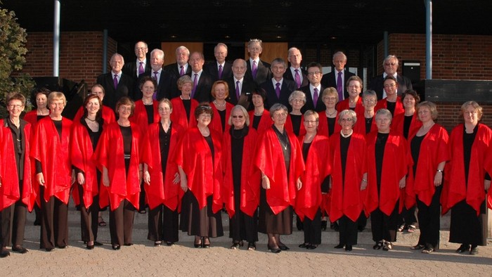 En gruppe af korister i røde kapper og mænd i formelle klæder står sammen udenfor et murværk