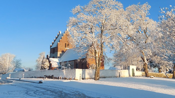 En snødekt landsby med en kirke og træer under et klart blå himmel.