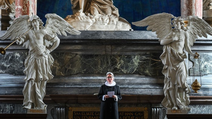 En præst står i en prægtig kirke med store skulpturer og billeder af engle.