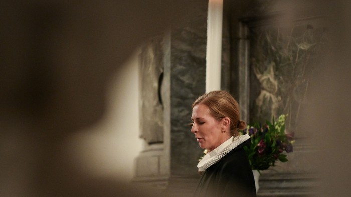 En kvinde i kirke med lysende candel og blomster.