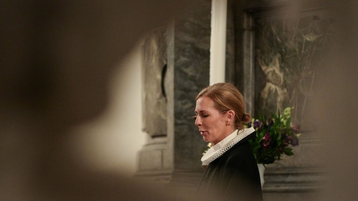 En kvinde i kirke med lysende candel og blomster.