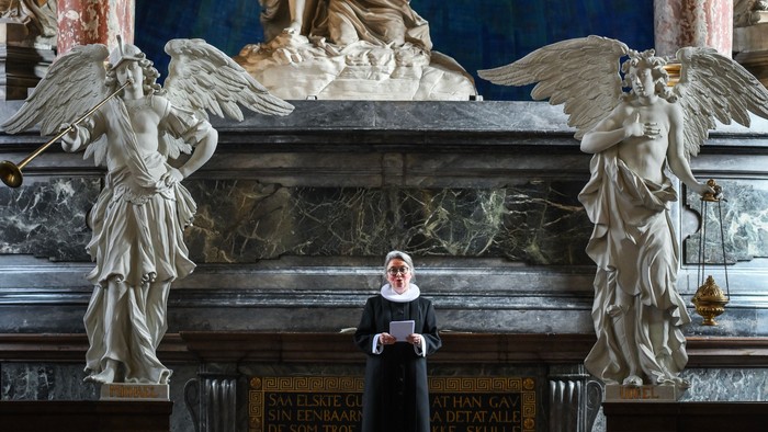 En præst står i en prægtig kirke med store skulpturer og malerier.