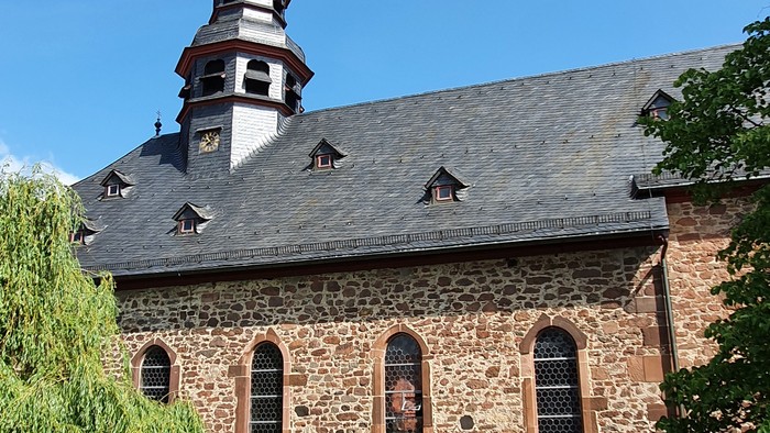 Alte Kirche mit hohem Turm und spitzem Dach, umgeben von Bäumen und grünem Gras