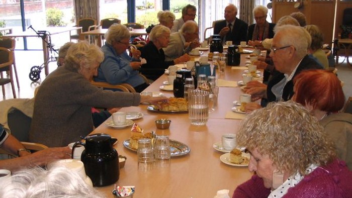 En gruppe pensionister sidder om en lang bord og spiser.