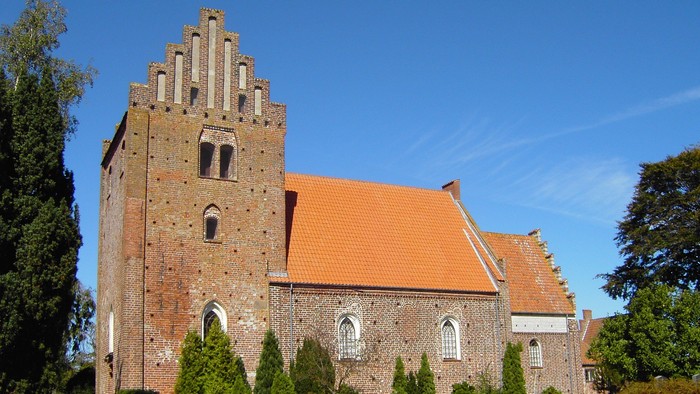 Gamle kirke med røde tag og mursten, omgivet af grønne planter og træer