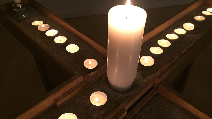 En lysende stålleker omgivet af flere mindre tealightlyser i en mørk, træagtig ramme.