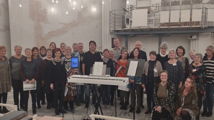 En gruppe af mænd og kvinder samlet om et piano og noter.