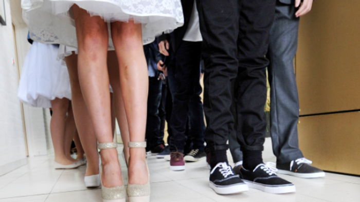 En brud og to mænd står sammen, brudens sko er høje og glitrende, mændenes sko er simple og mørke.