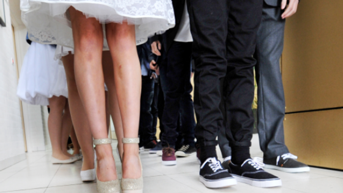 En brud og to mænd står sammen, brudens sko er høje og glitrende, mændenes sko er simple og mørke.