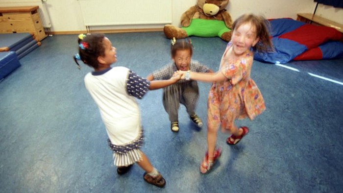 Drei Kinder spielen in einem Raum mit blauen Boden.