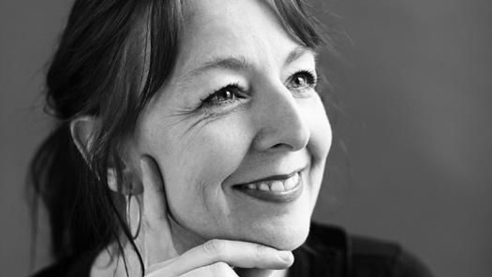 En svart-hvid portrætfoto af en kvinde med kort hår, der smiler og har håndene sammen.