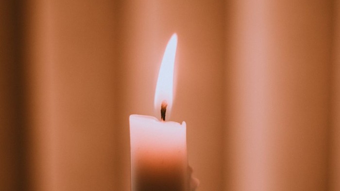 Eine brennende Kerze vor einem beigen Vorhang.