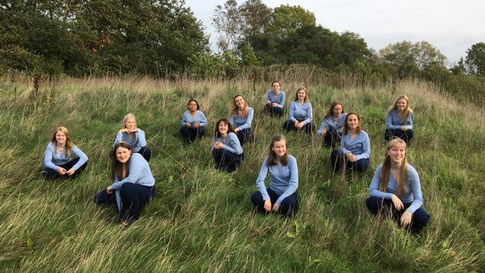 En gruppe unge piger sidder i højt græs i en naturlig omgivelse.