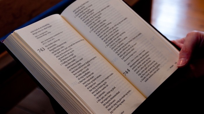 En hånd holder en åben bog, der viser en liste over navne og numre, sandsynligvis en Bibel med slægtsregistre.