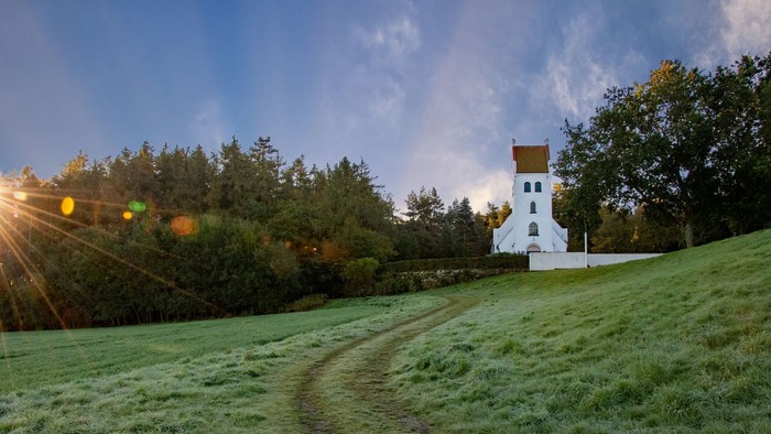 En lille hvidt malet kirke på en bakke med græs og træer i baggrunden
