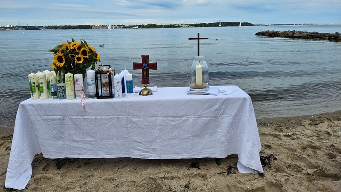 Ein Tisch am Strand mit Blumen, Kerzen und Kreuzen