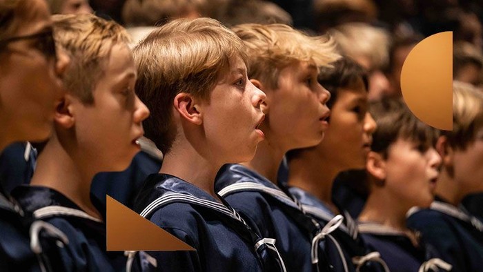 En gruppe drenge i mørke uniformer syng i kor.