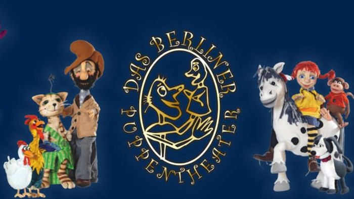 Das Bild zeigt eine Puppenbühne mit verschiedenen Figuren und einem Logo in der Mitte.