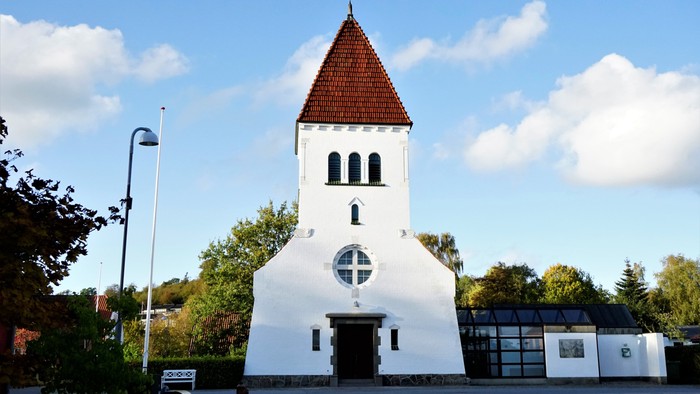 En hvid kirke med rød tagtårn og en rund vindueskærm.