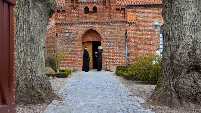 To ved en murstensgade til en kirke, hvor to personer står ved indgangen