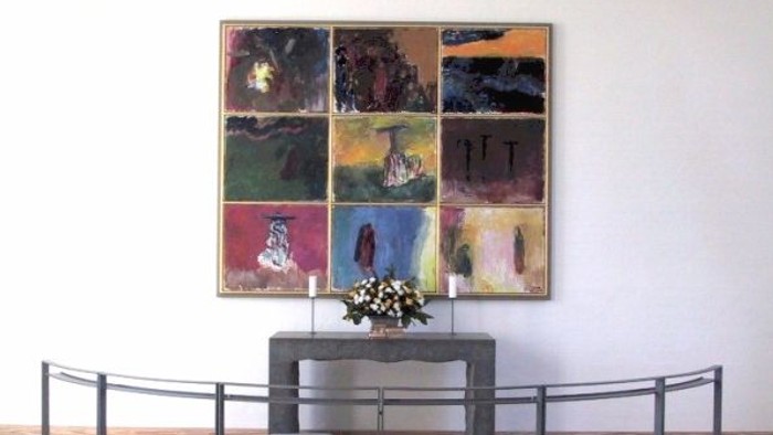 En stor maleriudstilling på væggen med en lille bord med blomster i forgrunden og en kurvet bænke foran