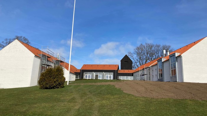 En hvid bygning med røde tag og en høj flagstang foran