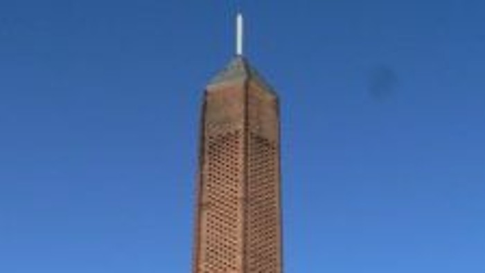 Hoher Backsteinkirchturm vor blauem Himmel.