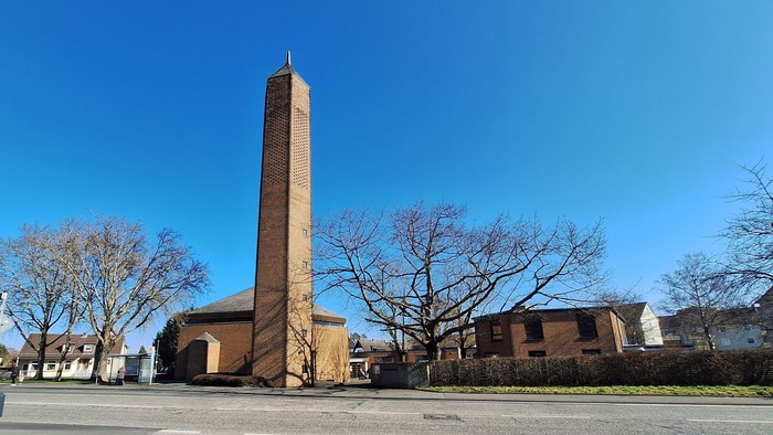 Hoher Ziegelobelisk vor einer Kirche, klarer blauer Himmel