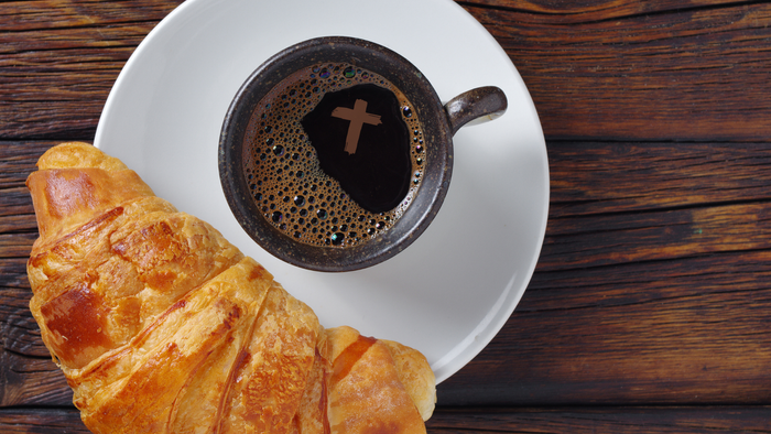 Un croissant doré à côté d'une tasse de café noir sur une assiette blanche