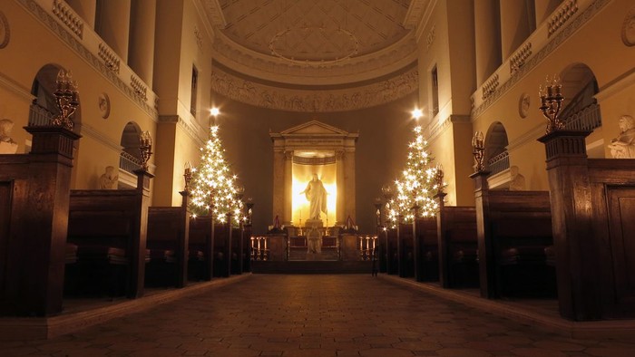 Indre del af en stor kirke med lysende kander og høje kolonner.