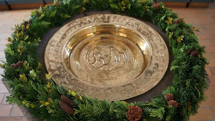 En stor gylden tra er placeret i midten af en grøn krans med nåletræer og kødbær.