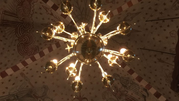 En stor belysning hænger fra taket med mønstre og malerier.
